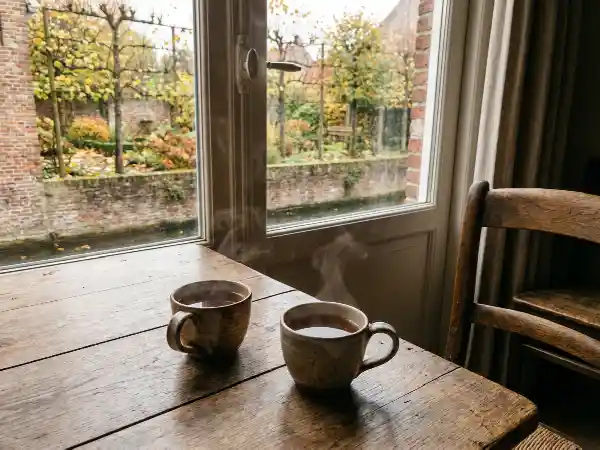 Twee kopjes thee op een tafel bij het raam met zicht op een herfsttuin
